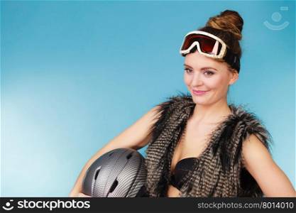 Woman seductive girl in ski googles holds helmet. Woman sexy hot skier girl wearing black bra fur vest ski googles holding helmet. Winter sport activity. Beautiful seductive sportswoman on blue studio shot