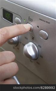 Woman Selecting Economy Program On Washing Machine To Save Energy