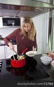 Woman serving pasta in bowl at kitchen counter
