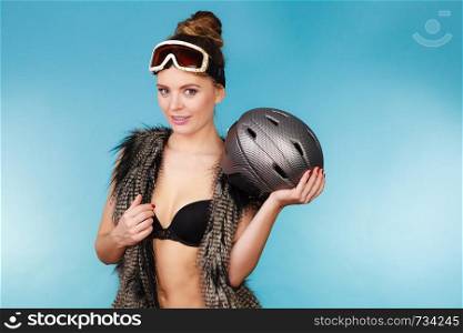 Woman sexy hot skier girl wearing black bra fur vest ski googles holding helmet. Winter sport activity. Beautiful seductive sportswoman on blue studio shot . Woman seductive girl in ski googles holds helmet