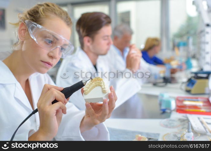 Woman shaping false teeth using an electric tool