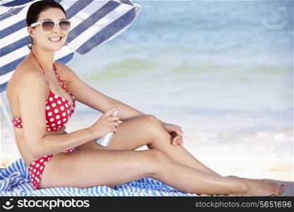 Woman Sheltering From Sun Under Beach Umbrella Putting On Sun Cream