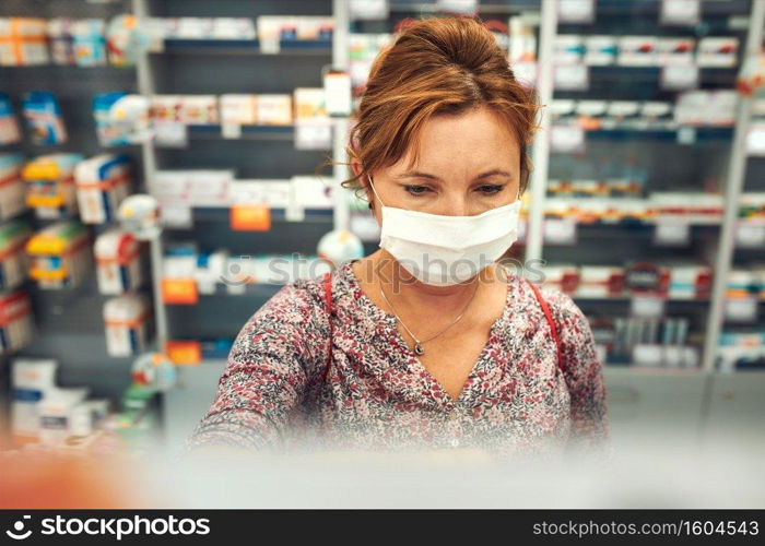 Woman shopping at pharmacy, buying medicines, wearing face mask to cover mouth and nose during pandemic coronavirus outbreak