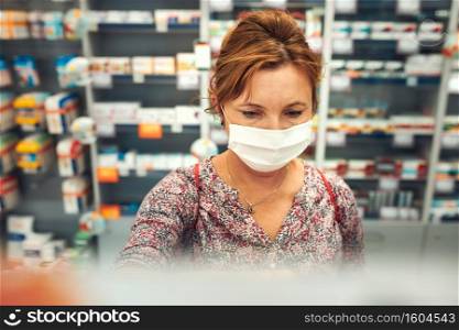 Woman shopping at pharmacy, buying medicines, wearing face mask to cover mouth and nose during pandemic coronavirus outbreak