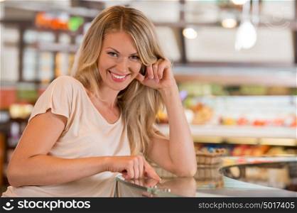 Woman shopping at the supermarket, standing near glass showcase and smiling at camera