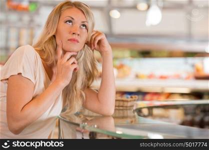 Woman shopping at the supermarket, standing near glass showcase and thinking what to choose