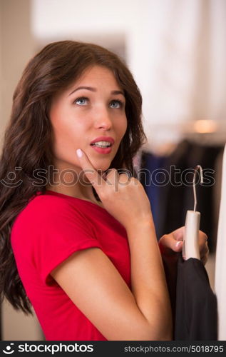 Woman shopping choosing dresses. Beautiful young shopper in clothing store.