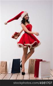 Woman shopping for christmas gifts. Young caucasian girl dancing with shopping bags wearing Santa Claus dress and hat