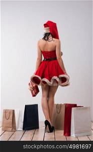 Woman shopping for christmas gifts. Young caucasian girl from behind with shopping bags wearing Santa Claus dress and hat