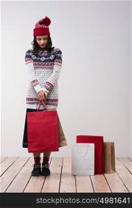 Woman shopping for christmas gifts. Young caucasian girl looking down shy with shopping bags and knitted hat. Copy space on the side.