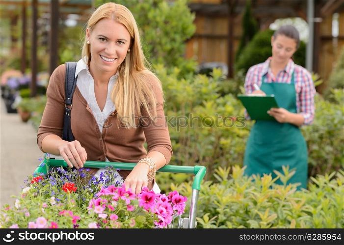 Woman shopping for flowers in garden center employee doing inventory