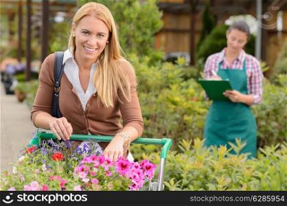 Woman shopping for flowers in garden center employee doing inventory