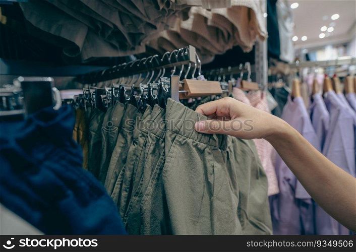 Woman shopping green shorts in clothing store. Woman choosing clothes. Shorts on hanger hanging on rack in clothing store. Fashion retail shop inside shopping mall. Clothes on hangers in clothes shop.