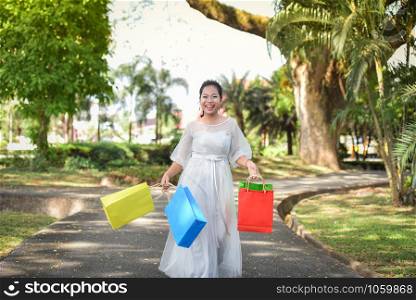Woman shopping on outdoors and hold shopping bags in hand / Asian woman laugh and happy in the park