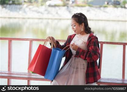Woman shopping on outdoors in the park / Asian woman shocked and glad see shopping bags in hand