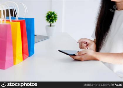 woman shopping online on mobile smart phone with colorful paper shopping bags