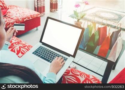 Woman shopping online using laptop with blank screen, credit card enjoying in home