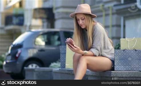 Woman shopping online using mobile phone outdoor. Cheerful woman sitting outdoors with shopping bags and shopping online.