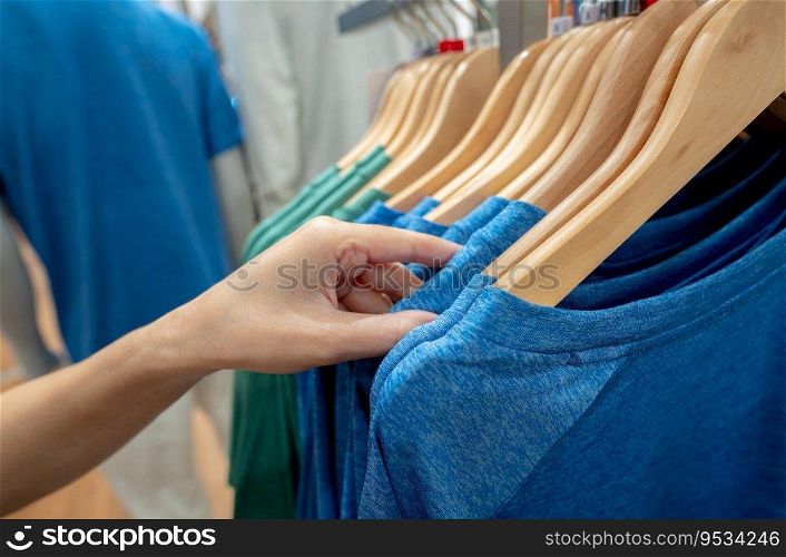 Woman shopping shirt in clothing store. Woman choosing clothes. Shirt on hanger hanging on rack in clothing store. Fashion retail shop inside shopping mall. Clothes on hangers in a clothes shop.