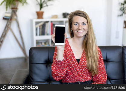 Woman showing a screen of a smart phone sitting on a sofa