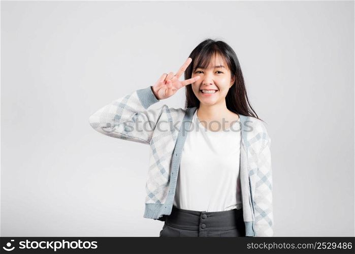 Woman showing finger making v-sign victory symbol near eye looking to camera, Happy Asian beautiful young female mark peace gesture symbol, studio shot isolated on white background with copy space
