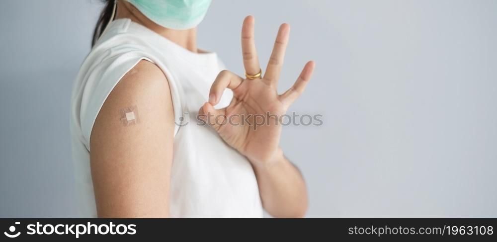 woman showing OK sign with bandage after receiving covid 19 vaccine. Vaccination, herd immunity, side effect, booster, vaccine passport and Coronavirus pandemic
