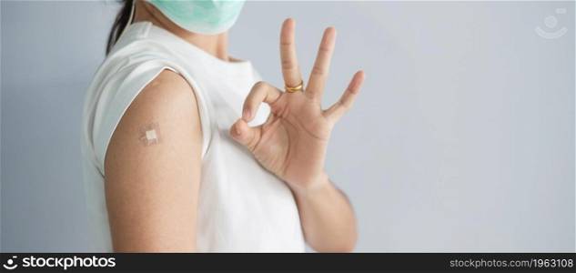 woman showing OK sign with bandage after receiving covid 19 vaccine. Vaccination, herd immunity, side effect, booster, vaccine passport and Coronavirus pandemic