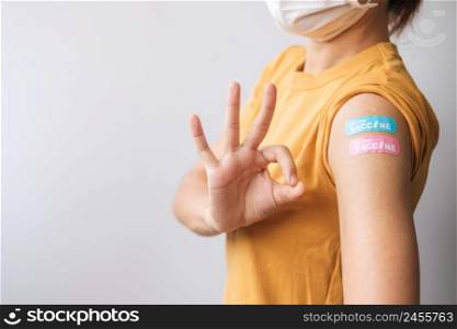woman showing OK sign with bandage after receiving covid 19 vaccine. Vaccination, herd immunity, side effect, booster dose, vaccine passport and Coronavirus pandemic