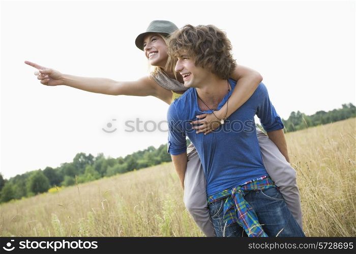 Woman showing something while enjoying piggyback ride on man in field