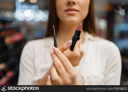 Woman shows lipstick and liner in cosmetics store. Buyer at the showcase in luxury beauty shop salon, female customer in fashion market. Woman shows lipstick and liner in cosmetics store