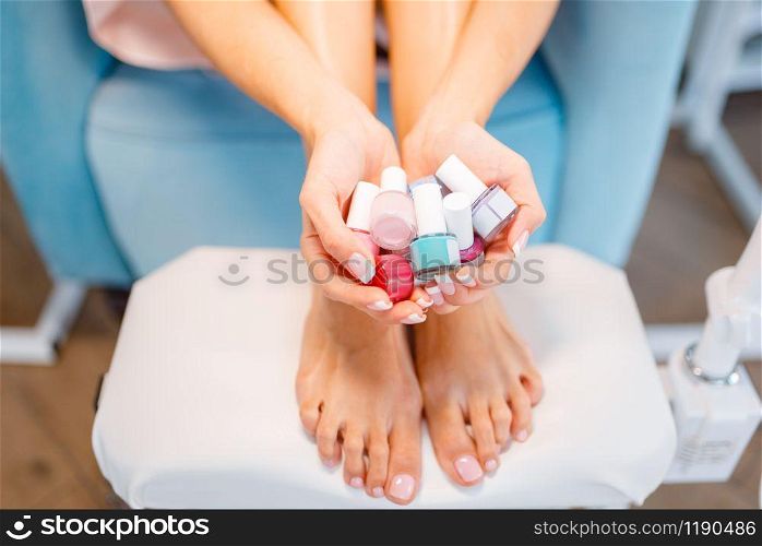 Woman shows many nail varnish bottles in beauty shop. Professional manicure and pedicure service, hands and legs treatment, client in beautician salon, female person at the cosmetologist