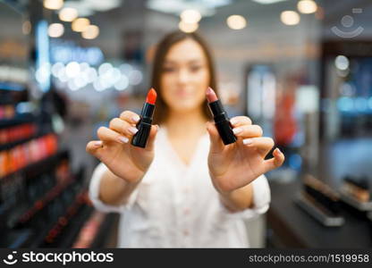 Woman shows two lipsticks in cosmetics store. Buyer at the showcase in luxury beauty shop salon, female customer in fashion market. Woman shows two lipsticks in cosmetics store