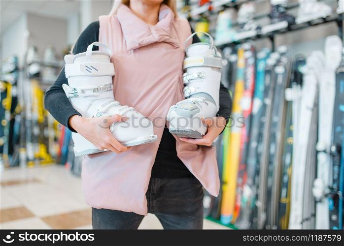 Woman shows white ski or snowboarding boots in sports shop. Winter season extreme lifestyle, active leisure, female customer with equipment. Woman shows ski or snowboarding boots, sports shop