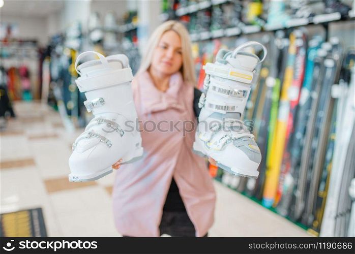 Woman shows white ski or snowboarding boots in sports shop. Winter season extreme lifestyle, active leisure, female customer with protect equipment