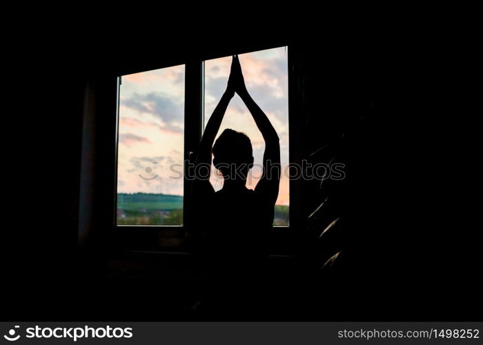 woman silhouette in yoga pose by window at sunet