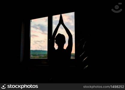 woman silhouette in yoga pose by window at sunet