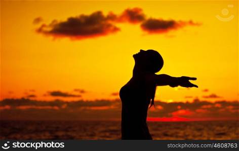Woman silhouette over sunset sky, dark black shadow of female body with hands up, teenage girl having fun outdoor, enjoying sundown on the beach, freedom lifestyle, happiness concept