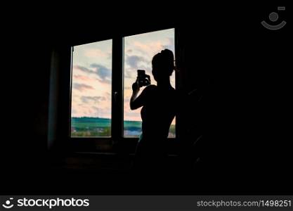 woman silhouette watching sunset from window quarantine concept