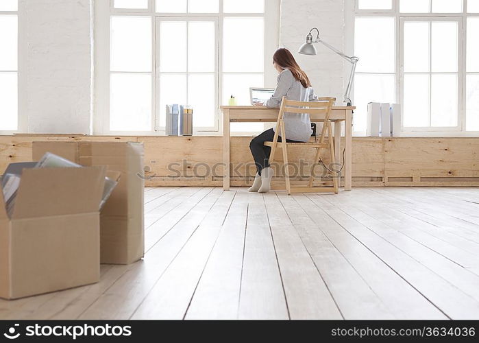 Woman sits at desk in window area of loft apartment