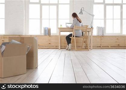 Woman sits at desk in window area of loft apartment