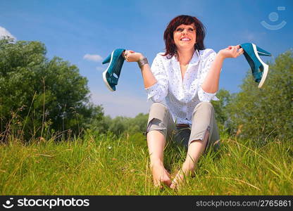 woman sits on grass and holds shoes in hands
