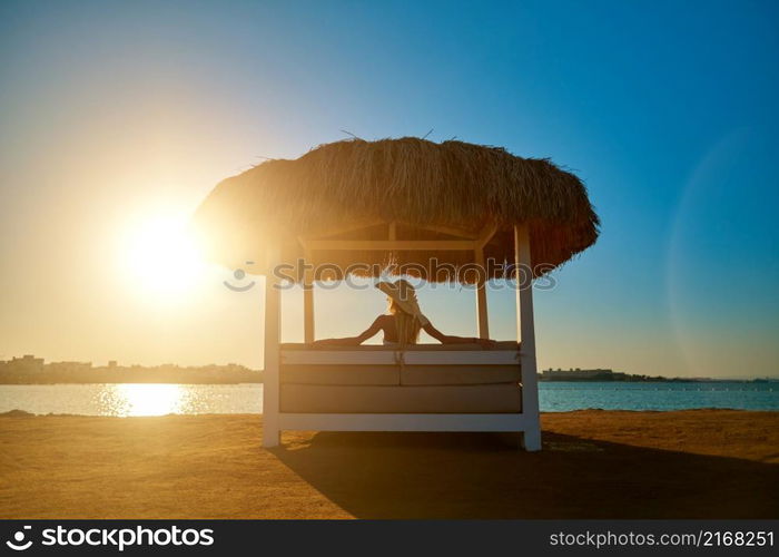 Woman sitting at Cabana with straw roof on a sandy beach on sunset.. Woman sitting at Cabana with straw roof on a sandy beach on sunset