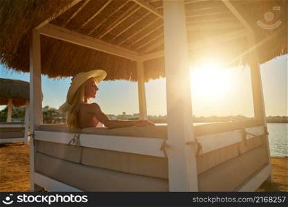 Woman sitting at Cabana with straw roof on a sandy beach on sunset.. Woman sitting at Cabana with straw roof on a sandy beach on sunset