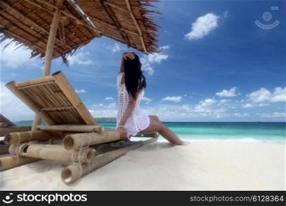 Woman sitting at chaise lounge with straw parasol on white sandy beach at Philippines. Woman sitting at chaise lounge