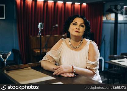 Woman sitting at table on microphone and piano background in restaurant