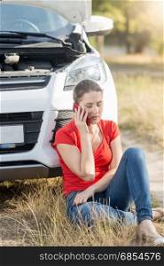 Woman sitting at the broken car and talking by phone