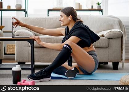 Woman sitting at the laptop, online fit training. Female person in sportswear, internet sport workout, room interior on background. Woman sitting at the laptop, online fit training