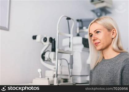 Woman sitting at the optician&rsquo;s office, modern medical equipment in the background. Oculist appointment.. Woman sitting at the optician&rsquo;s office