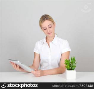 Woman sitting by green plant with electronic tablet