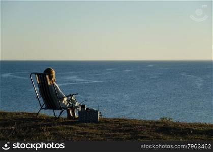 Woman sitting in a chair with a basket at seaside watching the blue sea
